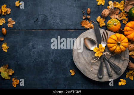 Thanksgiving background with cutlery on a wooden plate, small pumpkins and dry leaves on a blue wooden table. Top view Stock Photo