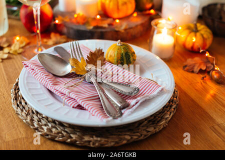 Thanksgiving table setting with old cutlery, small pumpkins, candles and orange lights garland in a rustic style Stock Photo