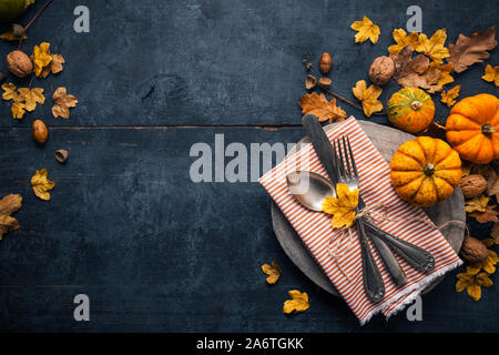 Thanksgiving background with cutlery on a wooden plate, small pumpkins and dry leaves on a blue wooden table. Top view Stock Photo