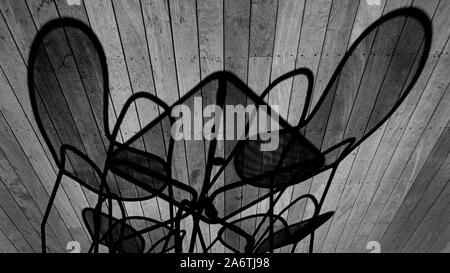 Shadows on wooden plank floor: Metal mesh chairs and a table cast an elongated shadow on wood patio floor. Stock Photo
