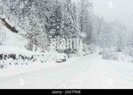 Snowy road among pine trees in winter with an SUV parked. Stock Photo