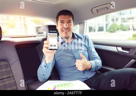 Mature businessman sitting on backseat of taxi rating cab services on app while commuting to work Stock Photo