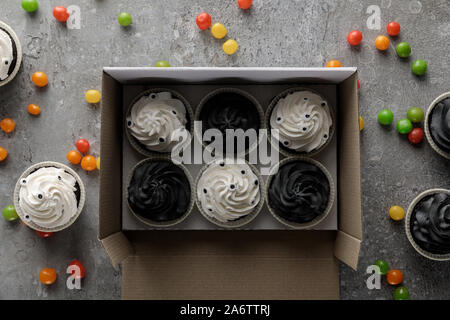 top view of delicious Halloween cupcakes in box near scattered colorful bonbons on concrete grey surface Stock Photo