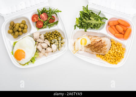 top view of eco packages with arugula, vegetables, meat, fried eggs and salad on white background Stock Photo