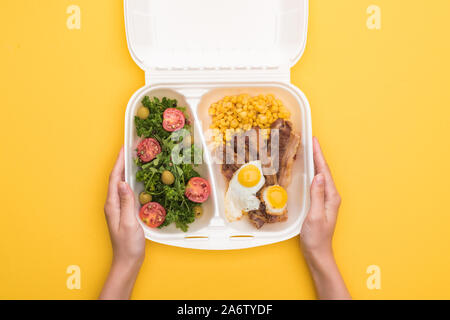 cropped view of woman holding eco package with corn, meat, fried eggs and salad isolated on yellow Stock Photo