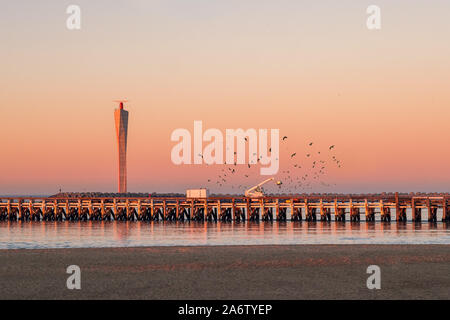 Sunset  on the old wooden pier of Ostend, with modern radar tower in the background. Lots of seagulls flying around. Stock Photo