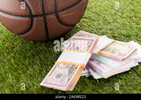 close up view of basketball ball near dollar and euro banknotes on green grass, sports betting concept Stock Photo
