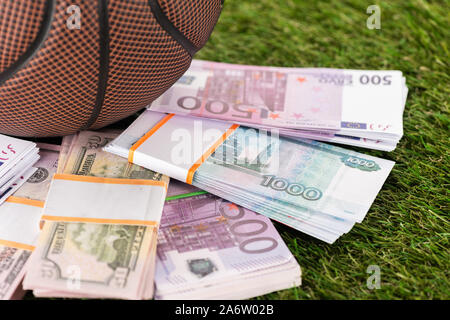 close up view of baseball ball near dollar and euro banknotes on green grass, sports betting concept Stock Photo