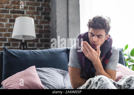 sick and handsome man in scarf coughing in bed