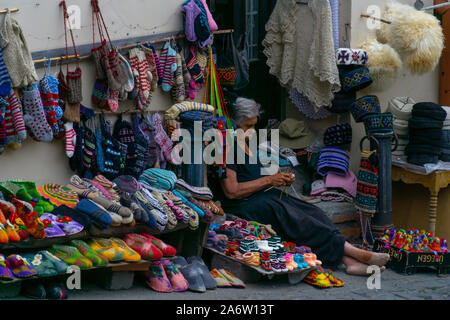 SIGNAGHI, GEORGIA - JULY 6, 2019: Georgian woman sits and sells on the street national rugs and knitted socks Stock Photo