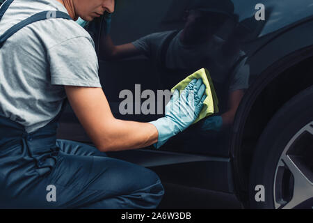 partial view of car cleaner polishing black car with rag Stock Photo