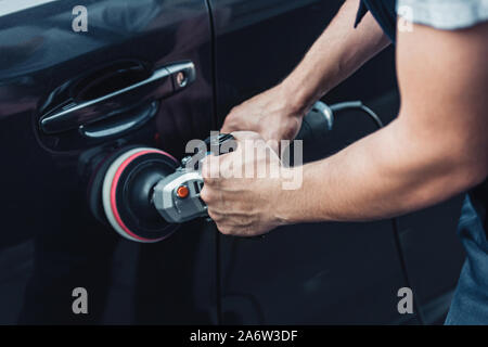 partial view of car cleaner polishing black car door with buffer machine Stock Photo