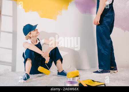 attractive young painter in uniform sitting on floor and looking at man in uniform Stock Photo