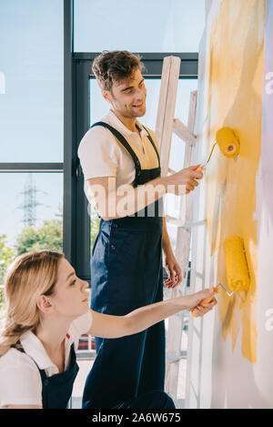 two young painters painting wall in yellow with paint rollers Stock Photo