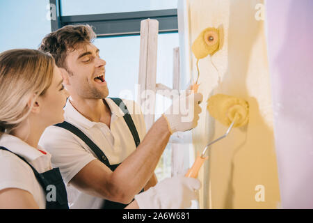 two young painters painting wall in yellow and pink with paint rollers Stock Photo