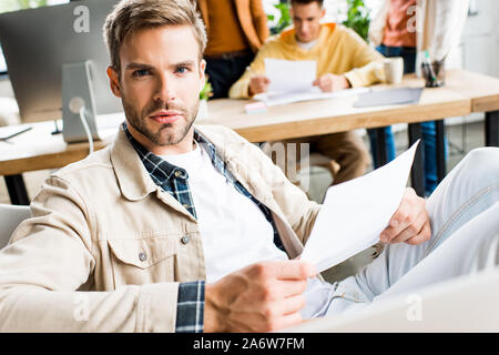 young businessman looking at camera while sitting at workplace in office Stock Photo