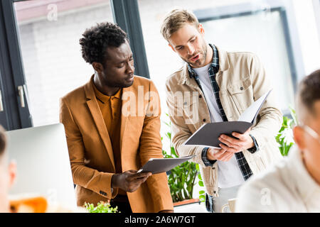 selective focus of young multicultural businessmen looking in folders in office Stock Photo