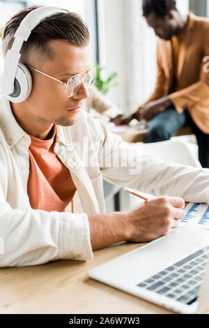 serious businessman in headphones analyzing graphs and charts and using laptop in office Stock Photo