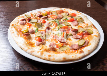Cheap pizza with sausages, cucumbers, cherry tomatoes, and herbs. Stock Photo