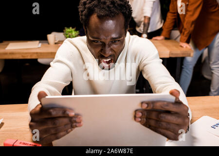 angry african american businessman looking at laptop while working at night in office Stock Photo