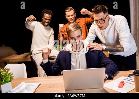 happy multicultural businesspeople showing winner gesture while working at night in office Stock Photo