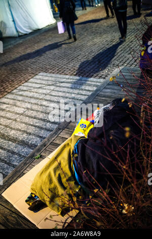Strasbourg, France - Dec 27, 2017: Winter scene with homeless man sleeping on the street with indifferent pedestrians walking on the cobblestone pavement Stock Photo