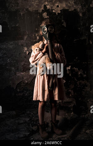 kid in gas mask standing and holding teddy bear, post apocalyptic concept Stock Photo