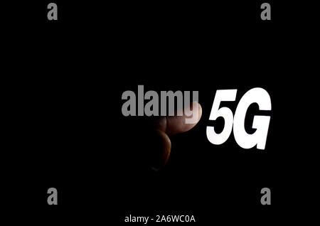5G letters glowing on the smartphone screen and the hand reaching for it. The concept photo for 5G wireless network. Stock Photo