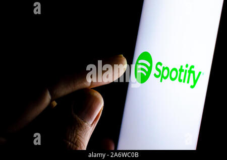Spotify logo on a smartphone screen in a dark room and a finger touching it. Stock Photo