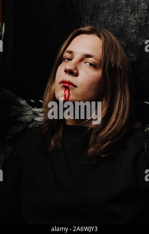 young long hair caucasian guy is going to go to a Halloween party in with makeup of blood from his mouth. Stock Photo