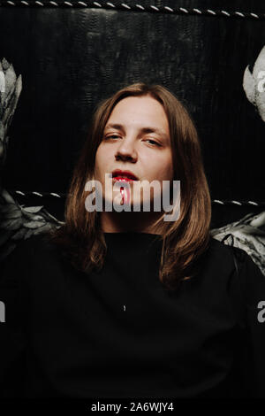 young long hair caucasian guy is going to go to a Halloween party in with makeup of blood from his mouth. Stock Photo