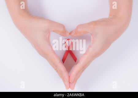 Woman hands forming a heart with her hands and a red ribbon for the fight against AIDS on a white background. Stock Photo