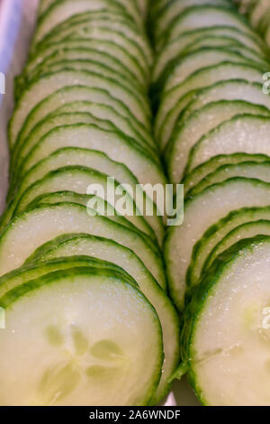 Two rows of sliced cucumber with their peels are viewed up close in their white serving tray. Stock Photo