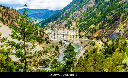Freight train on the railroad tracks running along the mighty Fraser River flowing in the Fraser Canyon in British Columbia, Canada Stock Photo