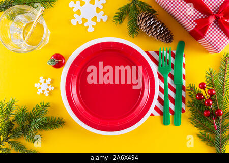 Fun Christmas kid's dinner table setting. Vibrant colors dishes, fork, napkin in holiday colors. Can be used as Option of New Year table setting. Stock Photo