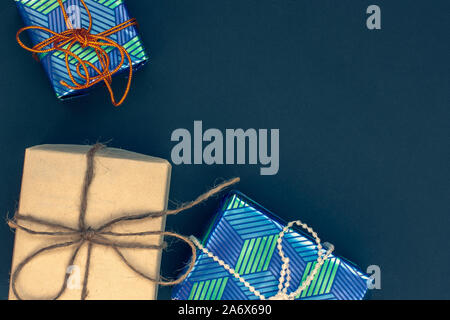 Three tied gift boxes with copy space on top right. One of kraft gray paper tied with hemp and two of blue gift paper. Yellow-blue tinting. Stock Photo