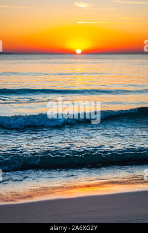 The sunset sun is going down behind the horizon. Tyrrhenian Sea bay with Elba island on the background at the sunset. Cala Violina beach, Scarlino, Pr Stock Photo