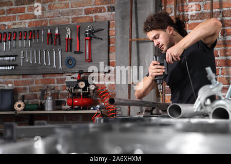 man in home workshop garage work drilling metal with drill, repair iron pipe on the workbench full of wrenches, diy and craft concept Stock Photo