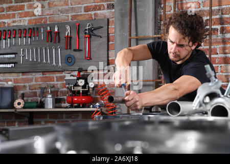 man work in home workshop garage with steel file rasp, filing metal pipe on the workbench full of wrenches, diy and craft concept Stock Photo