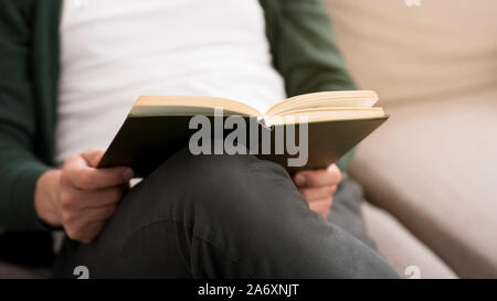 Cropped photo of man holding book, sitting on sofa Stock Photo