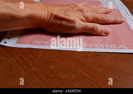 Closeup words private and confidential printed on continuous form paper with left hand pressing on it, selective focus Stock Photo