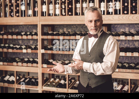 Sommelier Concept. Senior man standing showing wine smiling friendly Stock Photo