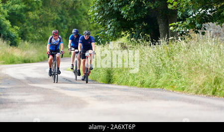 ROTHBURY, NEWCASTLE UPON TYNE, ENGLAND, UK - JULY 06, 2019: Three cyclists on a country road at the cyclone race event from Newcastle to Northumberlan Stock Photo