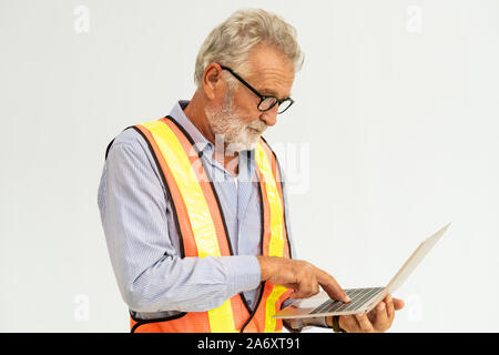 Experienced senior foreman or engineer using laptop computer standing against white background. Construction and engineering concept. Stock Photo