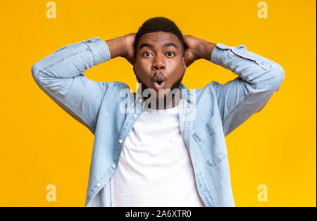 Amazed black guy holding hands behind head on yellow background Stock Photo