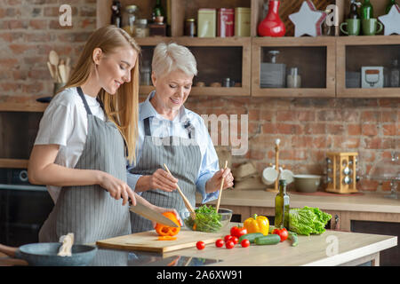 Young woman cooking healthy veggies salad with aged mom Stock Photo