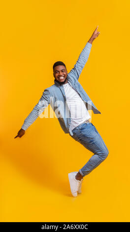 Cheerful African Man Standing On Tiptoes, Fooling Over Yellow Background Stock Photo