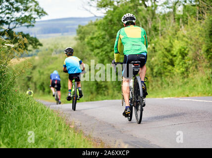 ROTHBURY, NEWCASTLE UPON TYNE, ENGLAND, UK - JULY 06, 2019: Three cyclists riding along a country lane at the cyclone race event from Newcastle to Nor Stock Photo