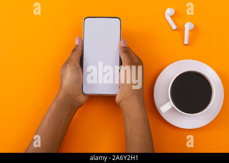 Female holding blank smartphone, using wireless earphones and drinking coffee Stock Photo