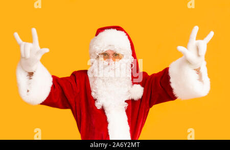 Young Santa in sun glasses showing horn sign on orange Stock Photo